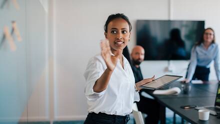 A professional at a white board, presenting the different jobs for master's in communication graduates to a man and a woman in a conference room.